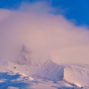 Pink mist swirling around a snowy mountain peak