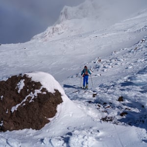 Skier climbing snowy slope toward foggy mountain peak