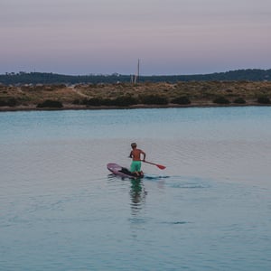 Boy paddleboarding on calm water at dusk