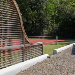 Curved wooden lattice screen beside red clay tennis court