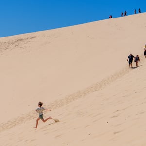 Boy running down sand dune under blue sky