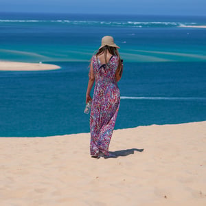 Woman in sun hat overlooking turquoise water from a dune