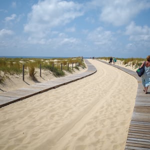 Two women walking wooden boardwalk through sunny sand dunes