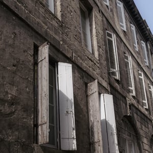 Weathered stone building with peeling white shutters