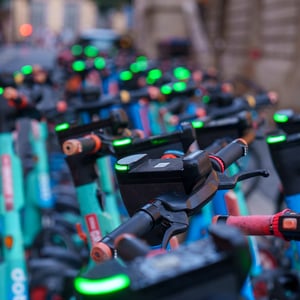 Row of teal electric scooters with green lights at dusk