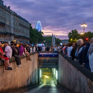 Crowds on stone walls above a glowing underpass at dusk