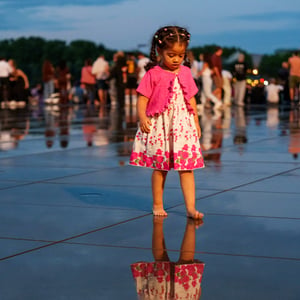 Girl standing barefoot on reflective plaza at dusk