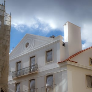 Whitewashed building with iron balconies under cloudy sky