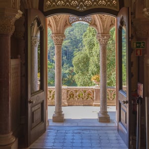 Gothic archway framing a sunlit stone terrace and forest