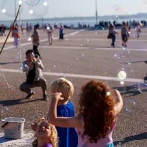 Kids chasing bubbles on a sunny waterfront promenade