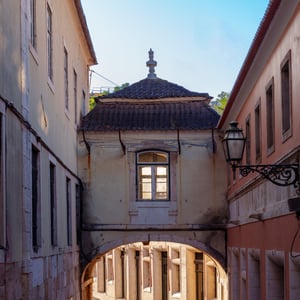 Sunlit cobblestone street under a stone arch
