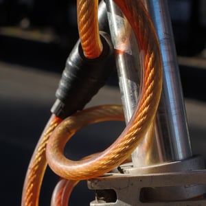 Orange braided bike cable lock wrapped around a metal post