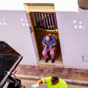 Man resting in doorway as waste collector emptying bin