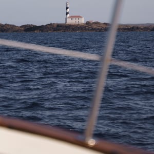 Striped lighthouse on rocky island seen from a boat