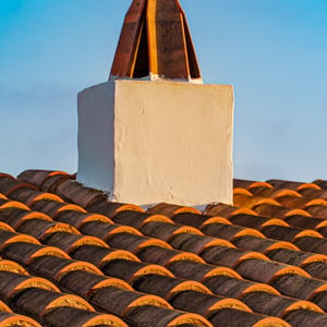 Whitewashed chimney with terracotta cap over clay roof tiles