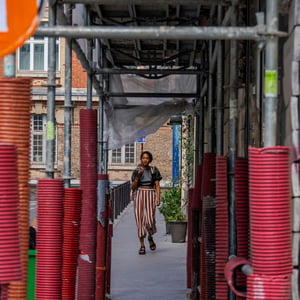 Woman walking past red pipes under urban scaffolding