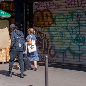 Pedestrians walking past colorful graffiti shutter in sunlight