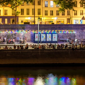Riverside cafés and crowds under rainbow lights at night