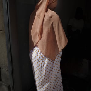 Woman in peach headscarf and polka dot skirt in doorway