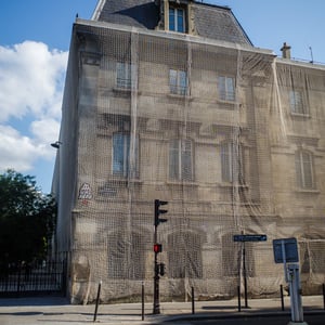 Paris building wrapped in beige netting under blue sky