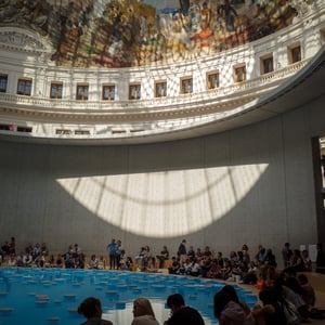 Visitors sitting beside a blue pool in a sunlit rotunda