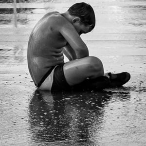 Boy sitting alone on wet pavement in black and white