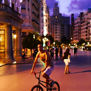 Man riding BMX bike through city square at dusk